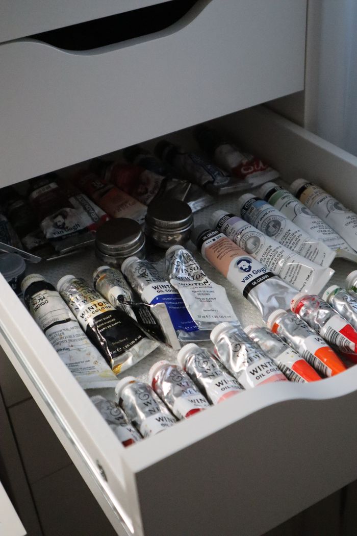 An open drawer filled with various tubes of oil paints and art supplies.